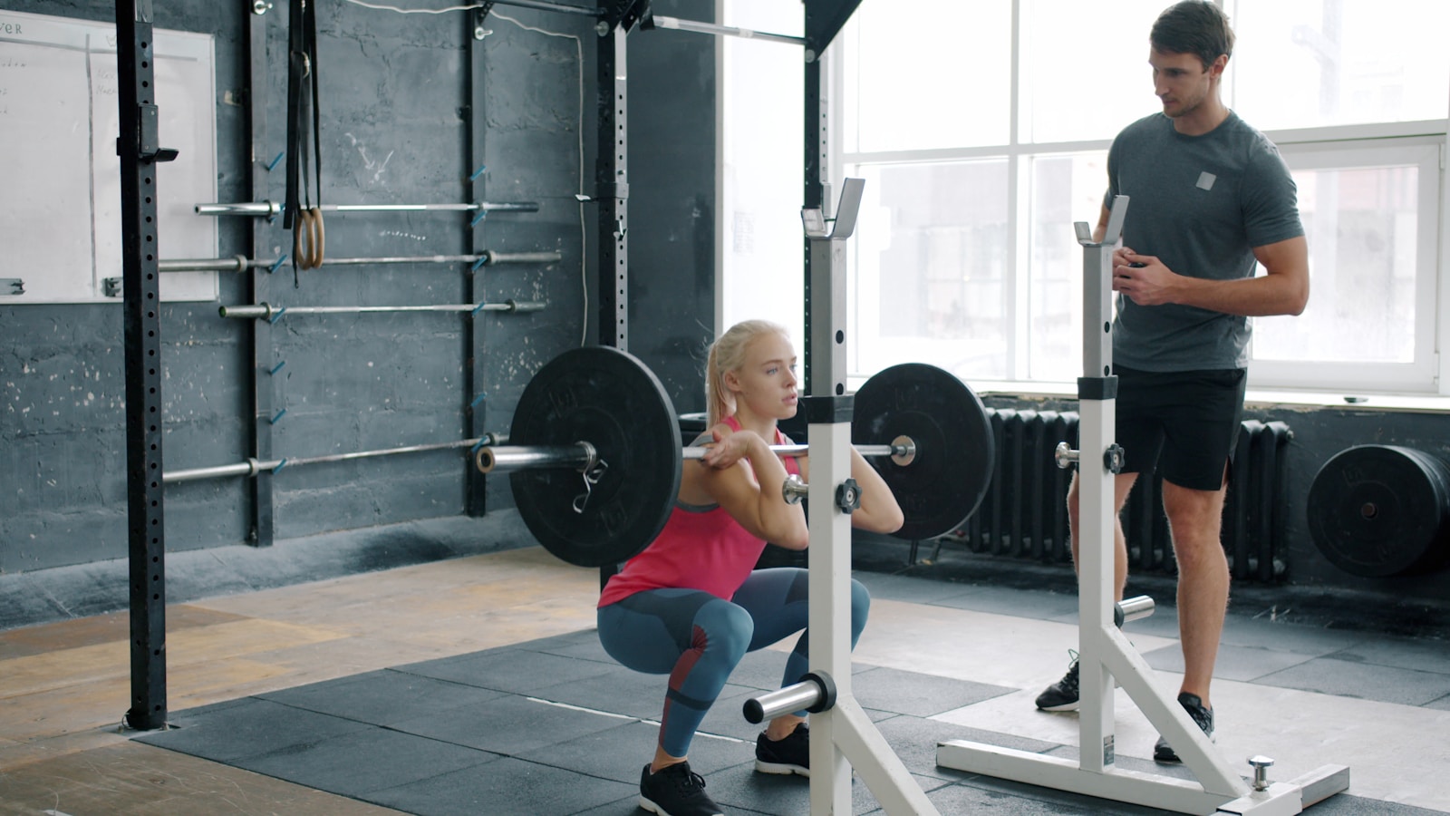 Coach helping a beginner learn safe squat technique in a gym